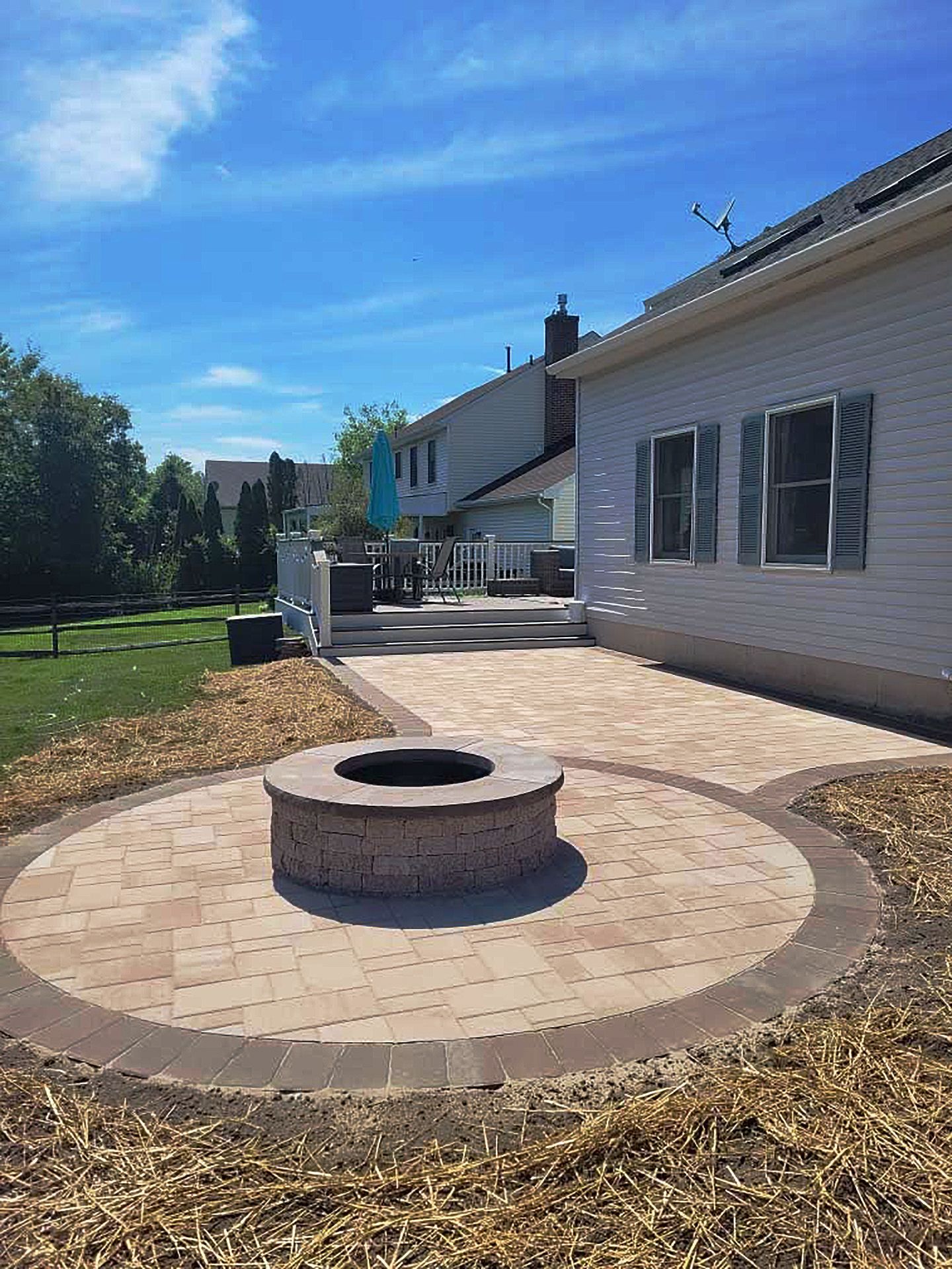 A fire pit is in the middle of a patio in front of a house.