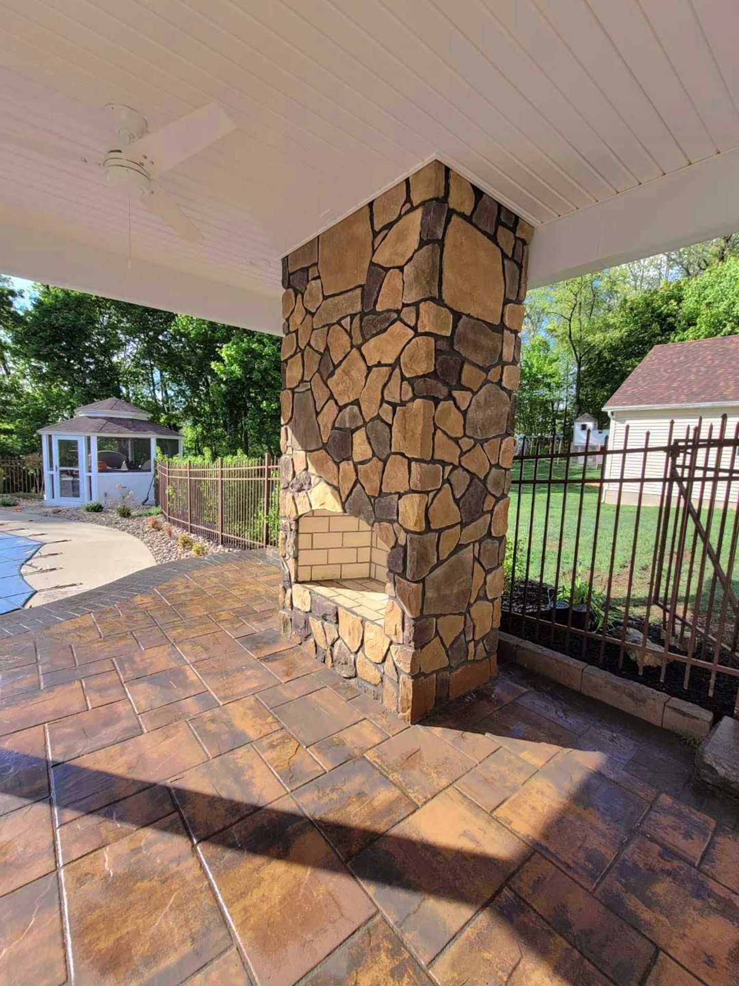 A patio with a stone column and a gazebo in the background.