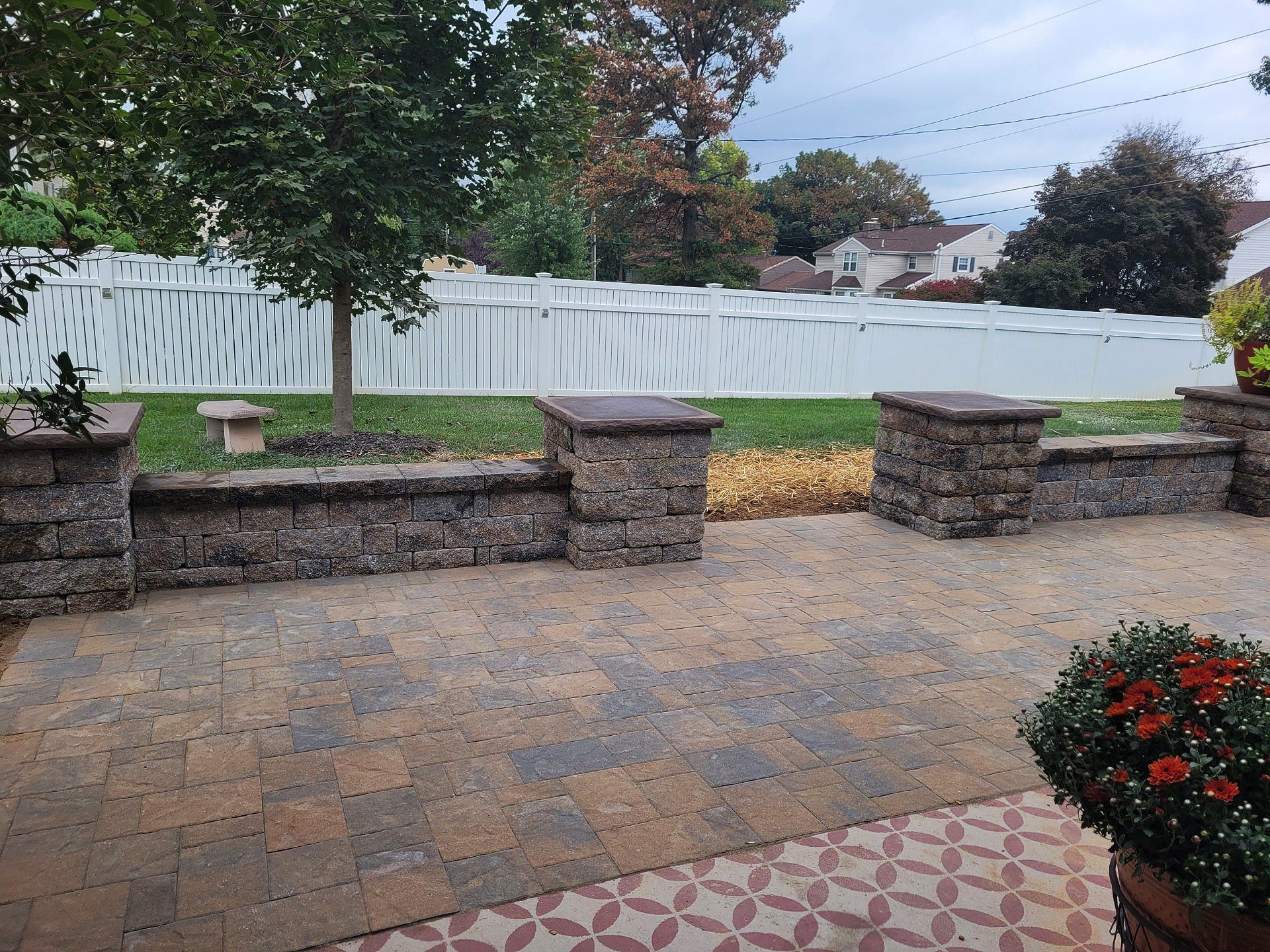 A patio with a stone wall and a white fence in the background.