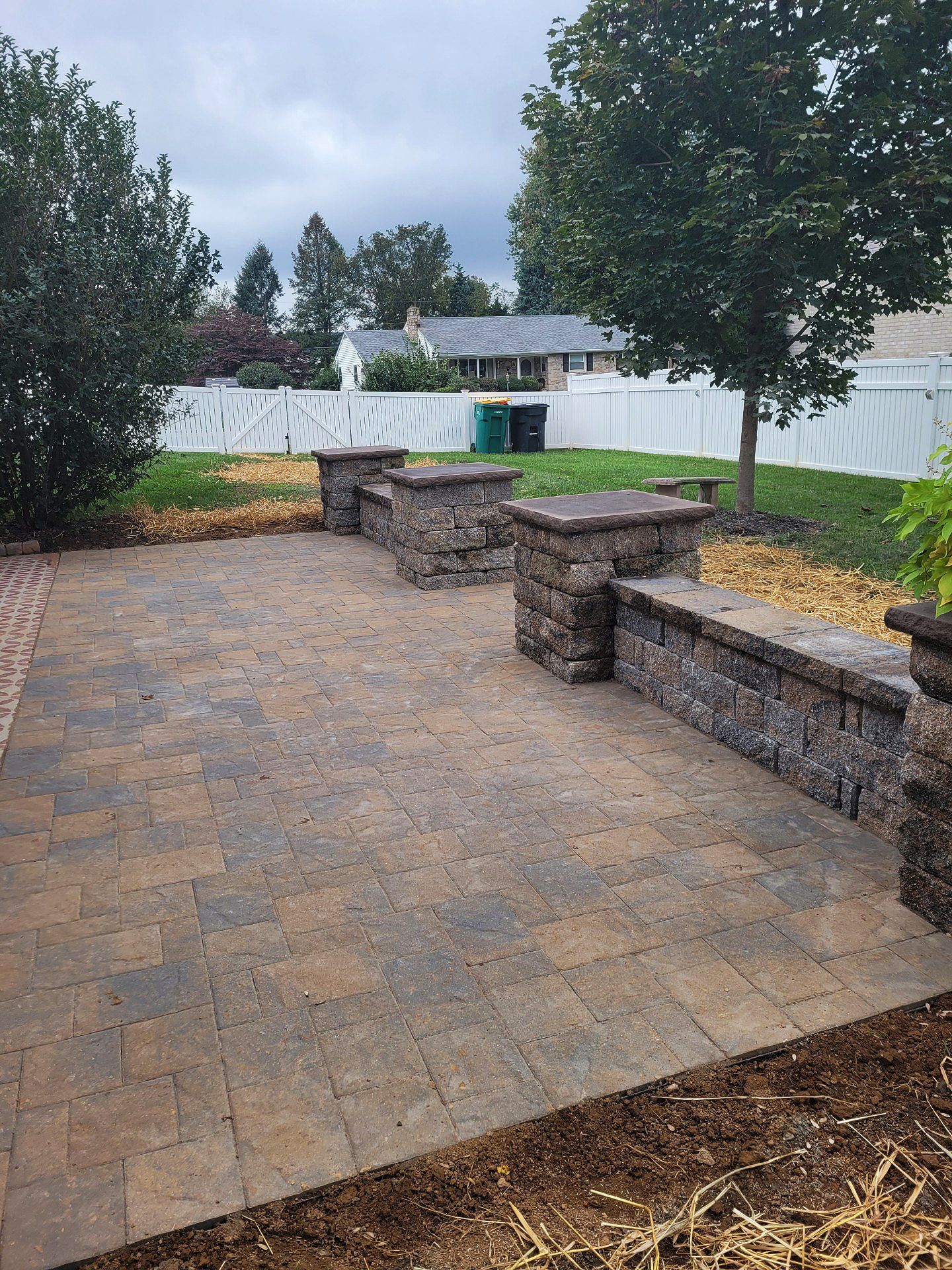 A patio with a stone wall and benches in the backyard of a house.