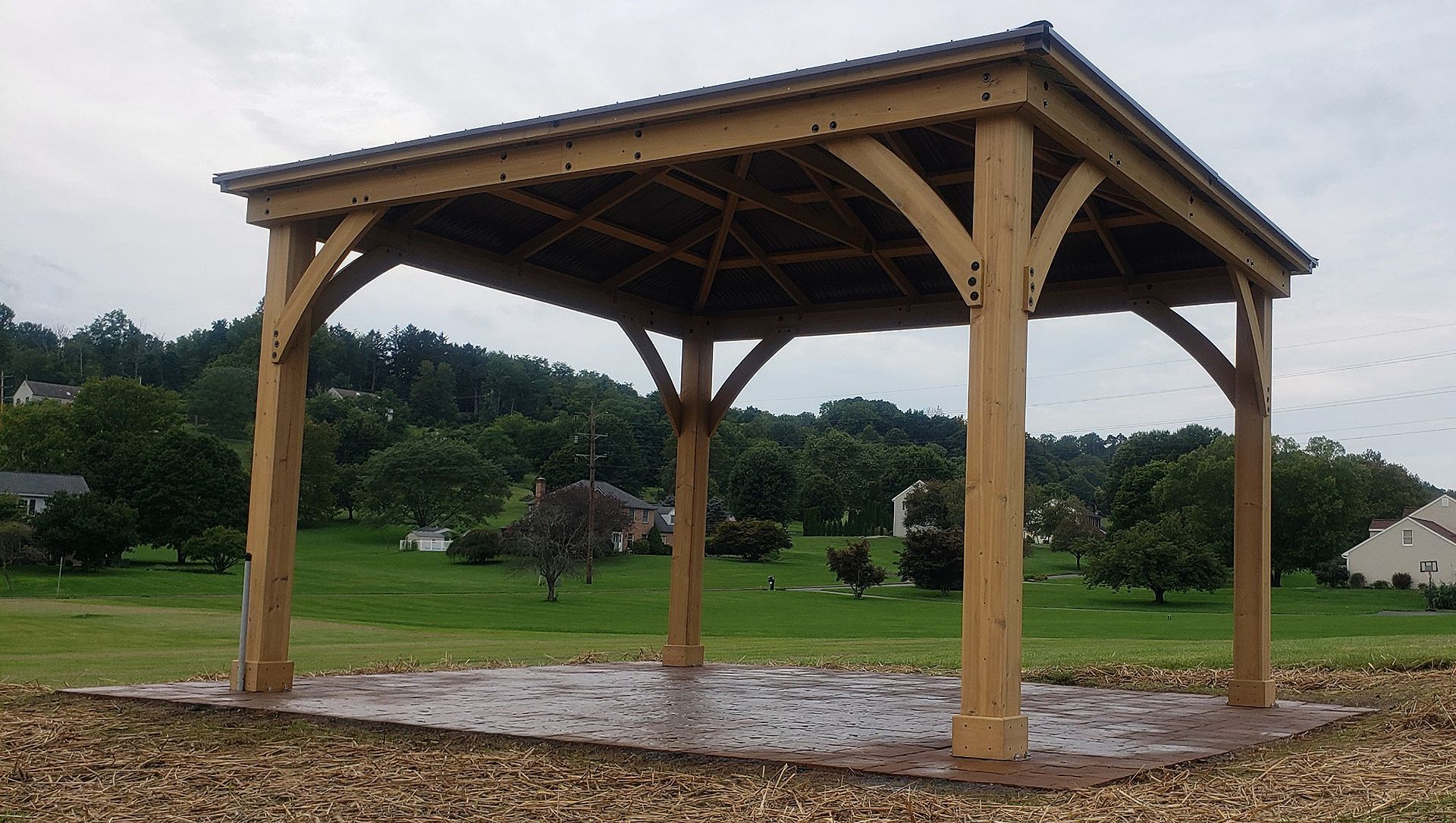 A wooden pavilion is sitting in the middle of a grassy field