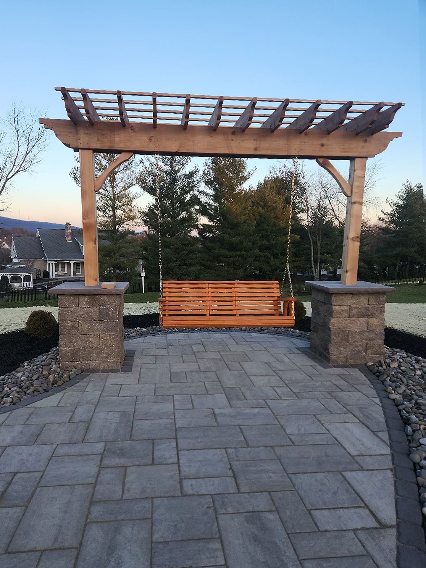 A wooden swing is sitting under a wooden pergola on a patio.