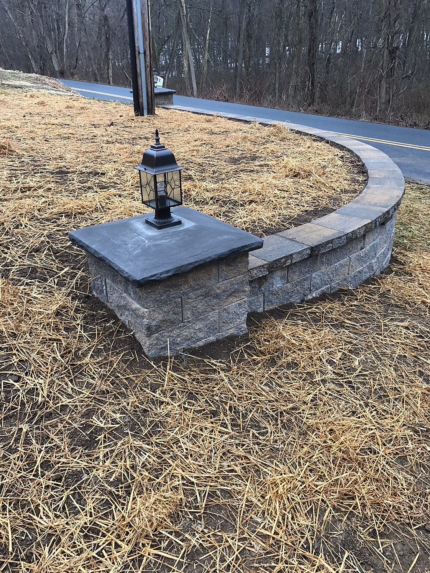 A lantern is sitting on top of a stone wall next to a road.