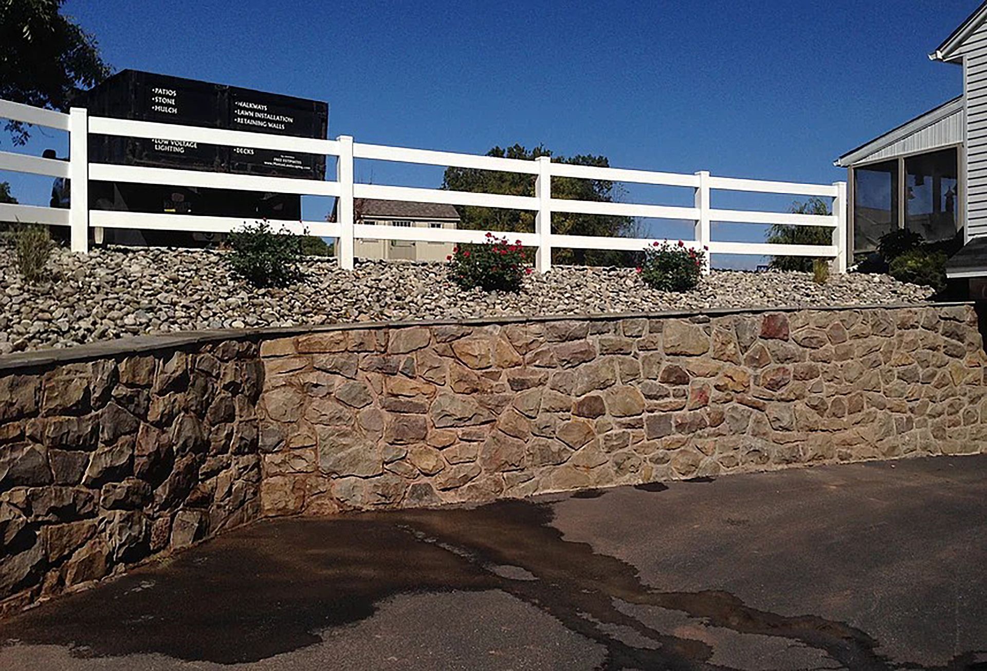 A white fence surrounds a stone wall in front of a house