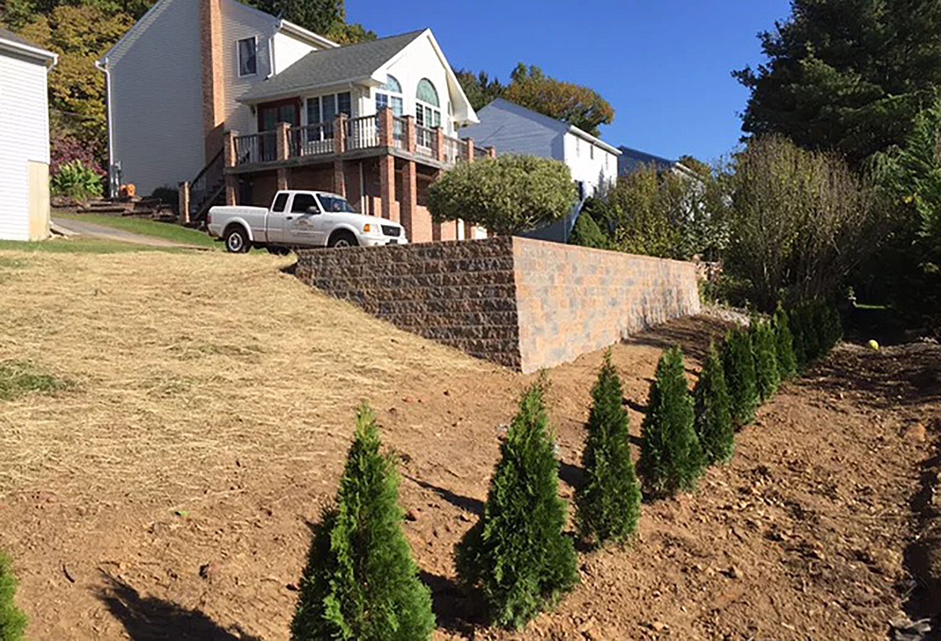 A white truck is parked in front of a house on a hill.