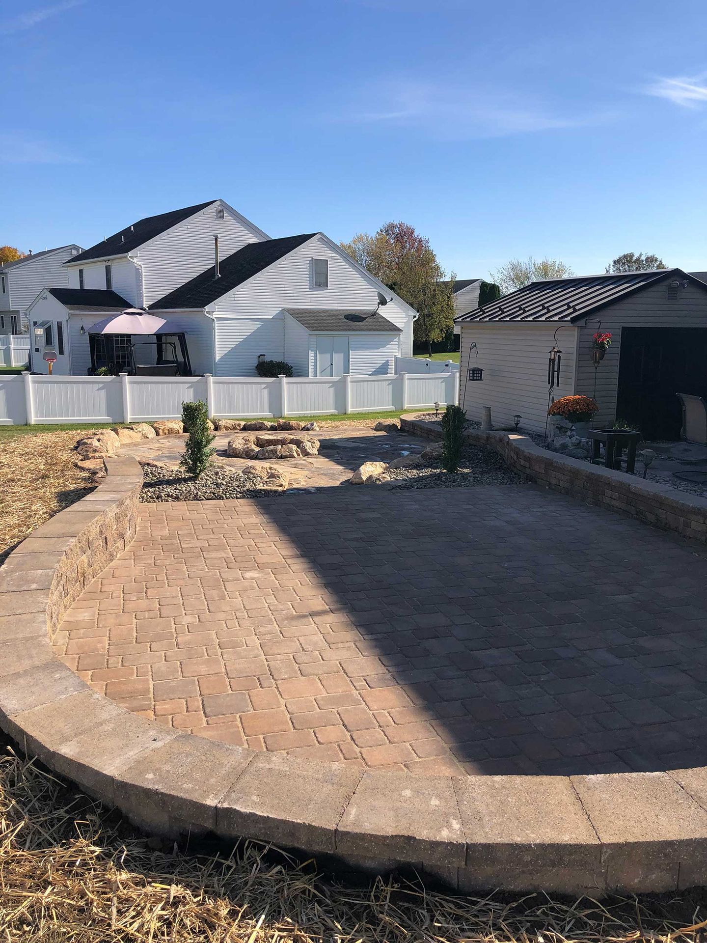 A brick walkway leading to a house with a white fence in the background.