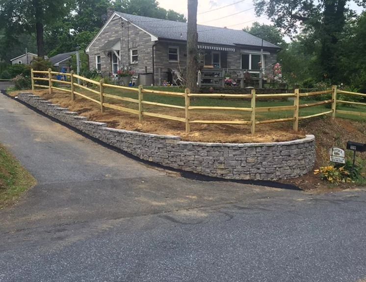 A wooden fence surrounds a stone wall in front of a house