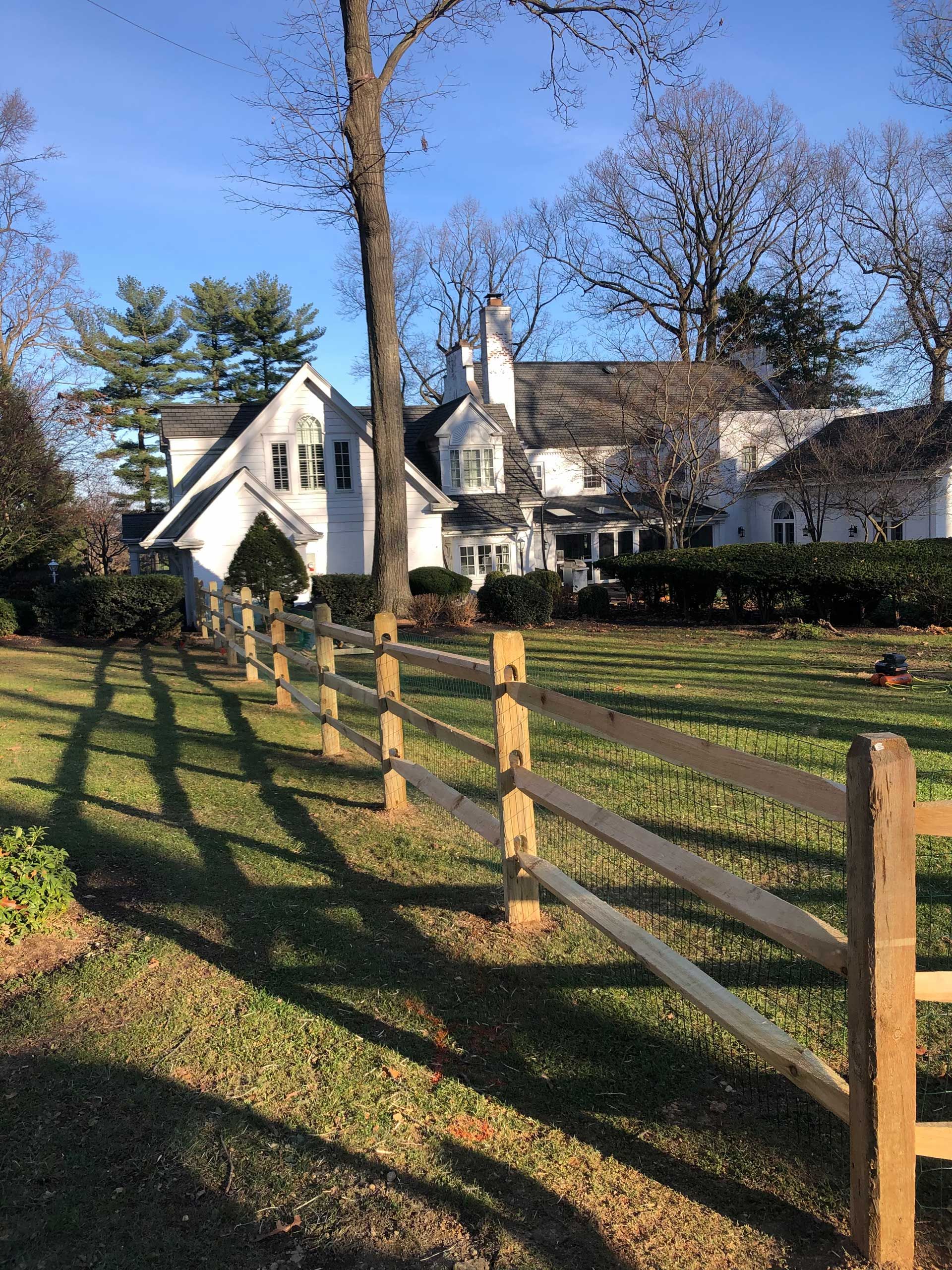 A wooden fence surrounds a grassy field in front of a large white house.