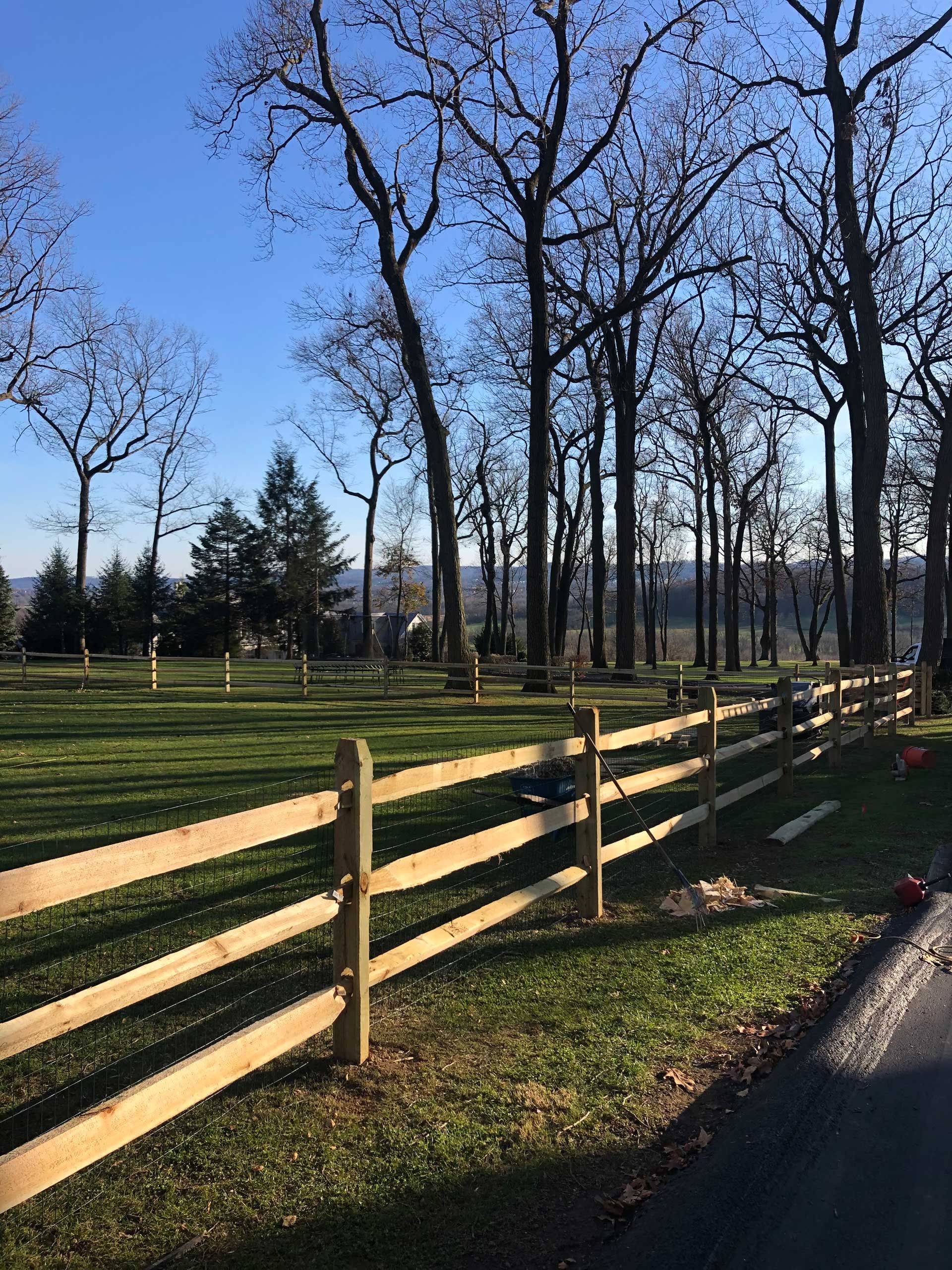 A wooden fence surrounds a grassy field with trees in the background.