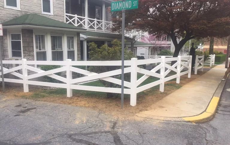 A white fence surrounds a sidewalk in front of a house.