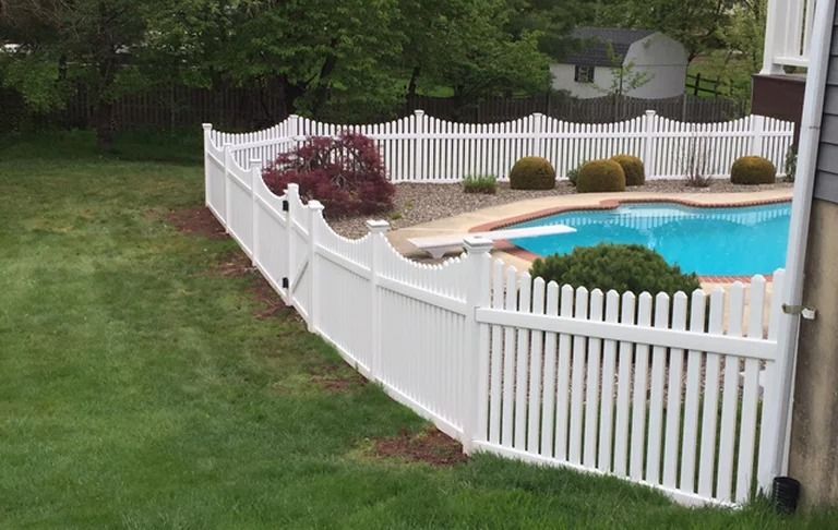 A white picket fence surrounds a swimming pool in a backyard.