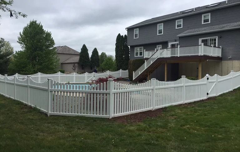 A white fence surrounds a swimming pool in front of a house.