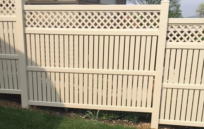 A white fence with a lattice design is sitting on top of a lush green lawn.