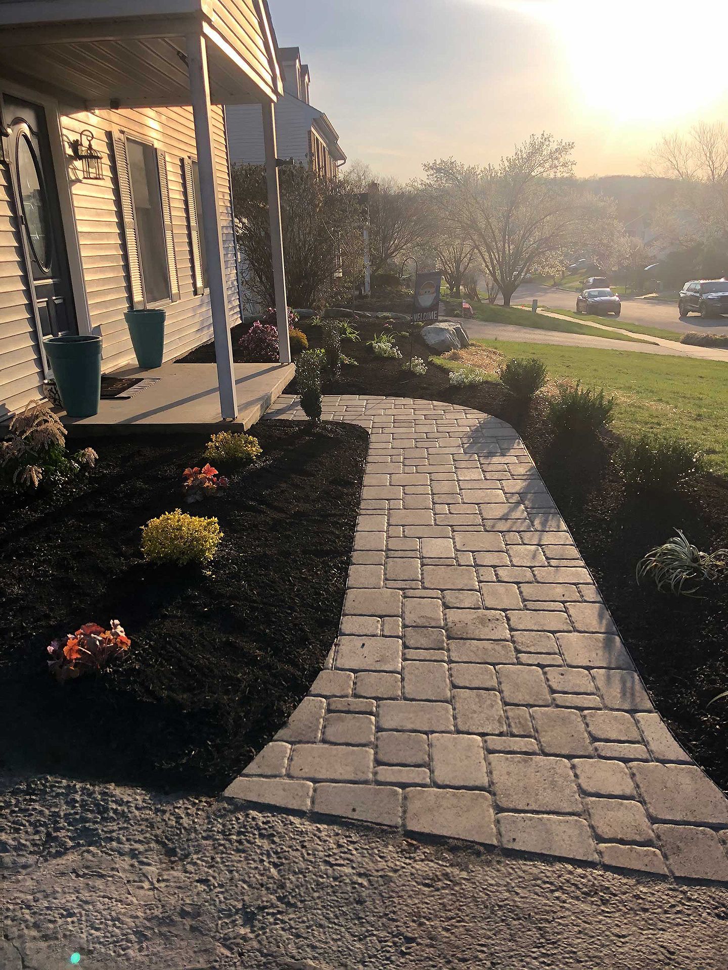 A brick walkway leading to a house with a sunset in the background.