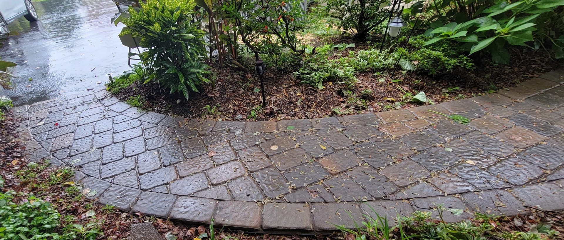 A brick walkway surrounded by trees and bushes on a rainy day.