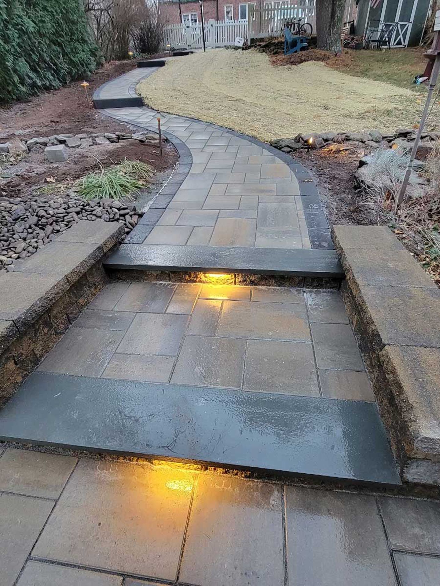 A stone walkway with lights on the steps in a backyard.