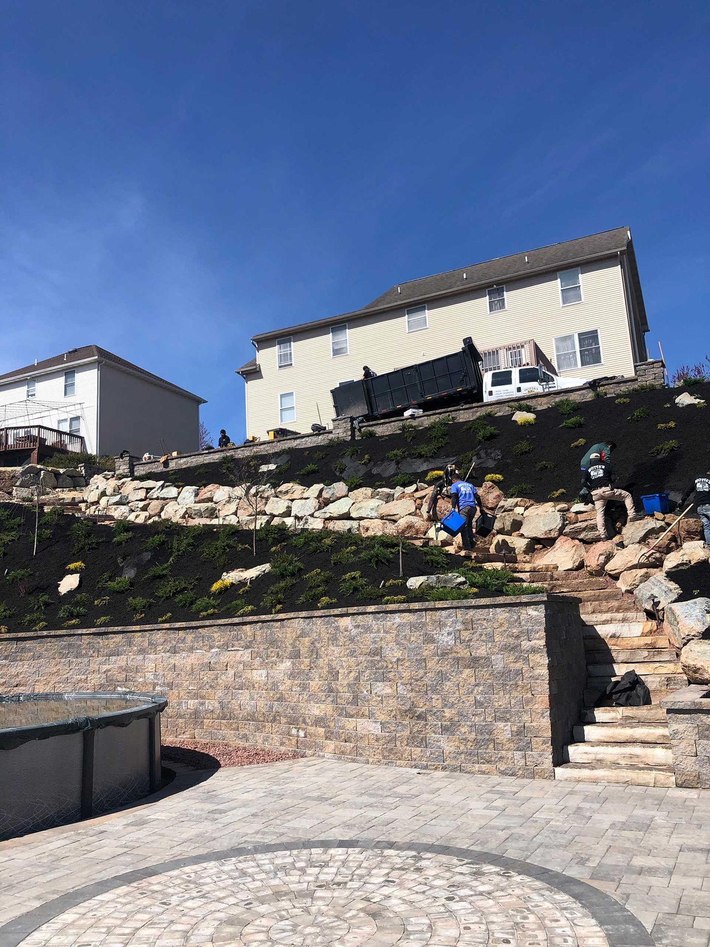 A large house is sitting on top of a hill next to a large rock wall.
