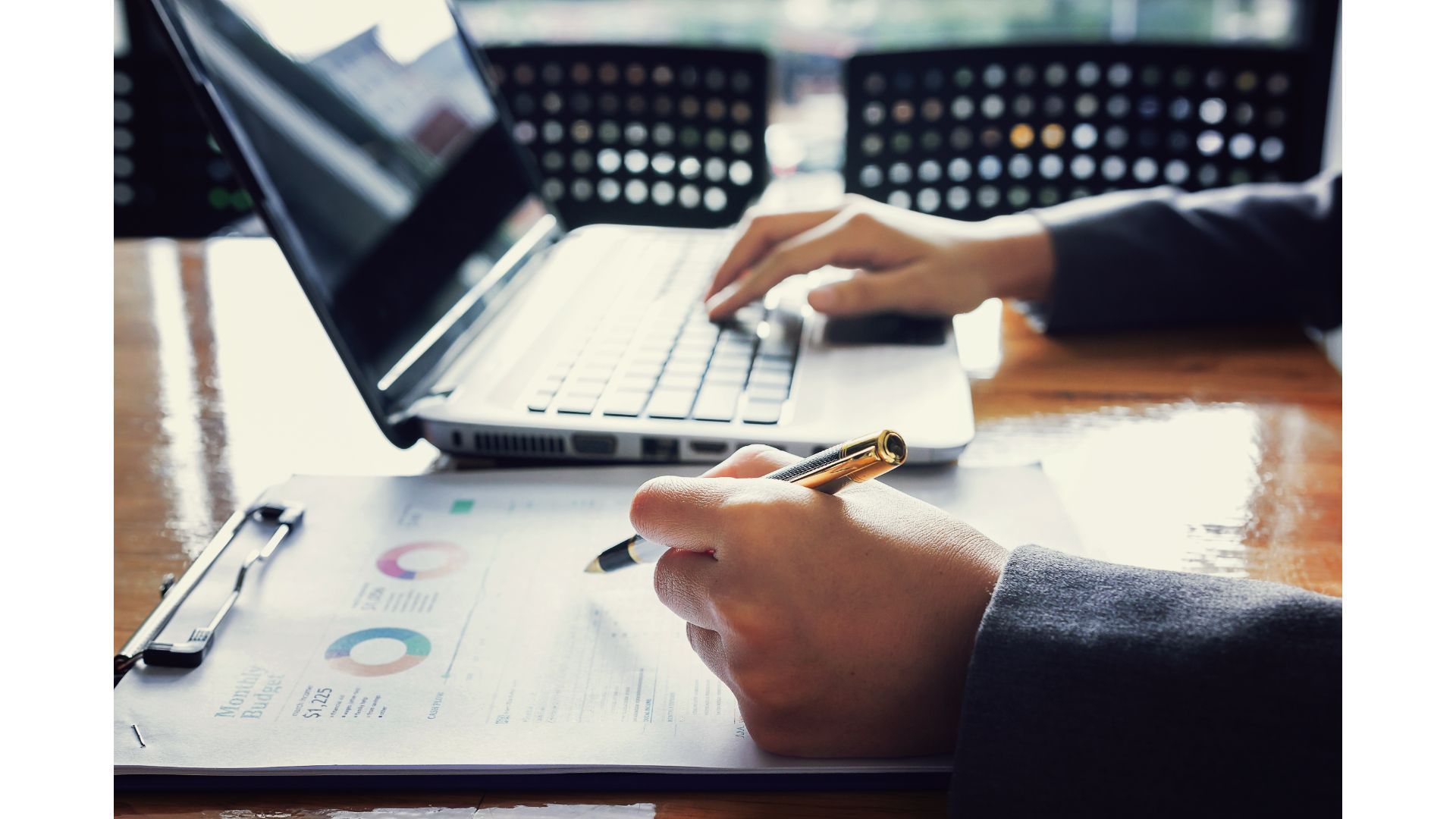 A person is typing on a laptop computer while holding a pen.