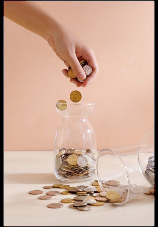A person is putting coins into a glass jar.