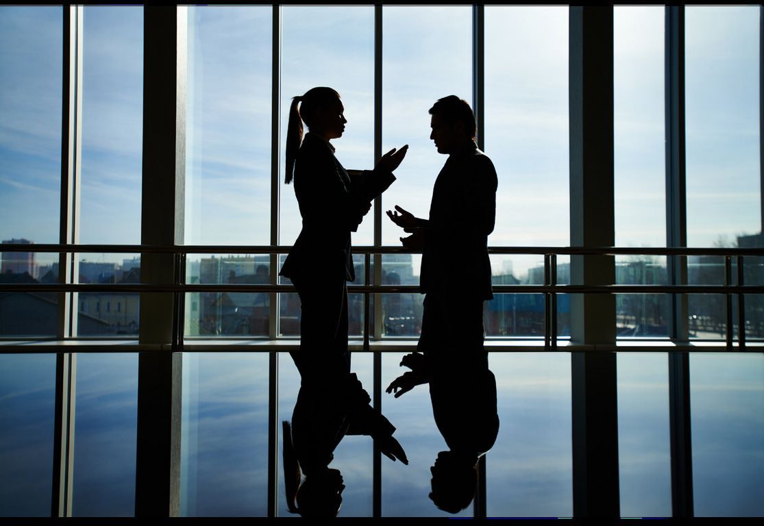 A man and a woman are standing in front of a window talking
