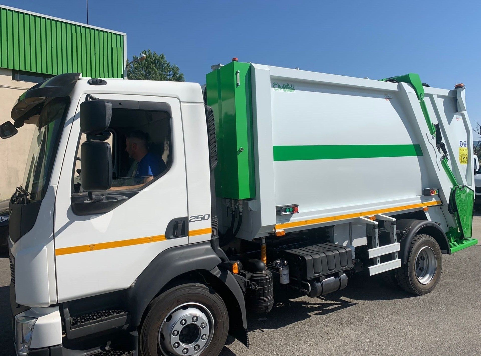Camion della spazzatura bianco e verde parcheggiato all'aperto in piena luce del sole.