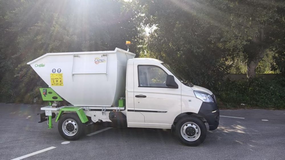 Camion bianco di servizio con attrezzature verdi parcheggiato su una strada soleggiata accanto agli alberi.