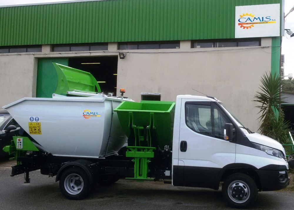Camion della spazzatura bianco con attrezzatura di carico verde parcheggiato fuori da un edificio
