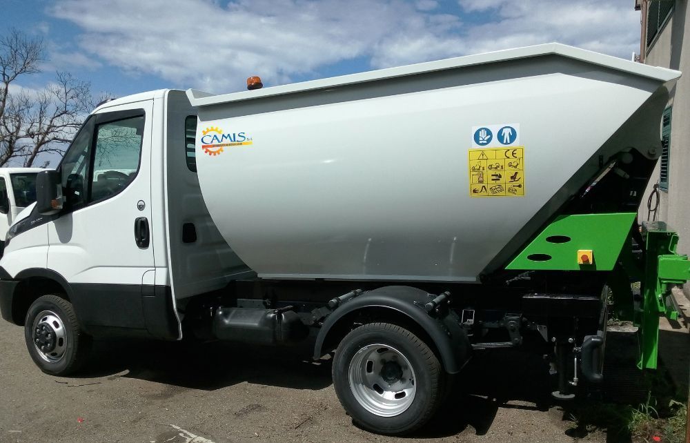 Camion della spazzatura bianco parcheggiato all'aperto sotto un cielo azzurro, con sponda idraulica posteriore verde e logo aziendale.