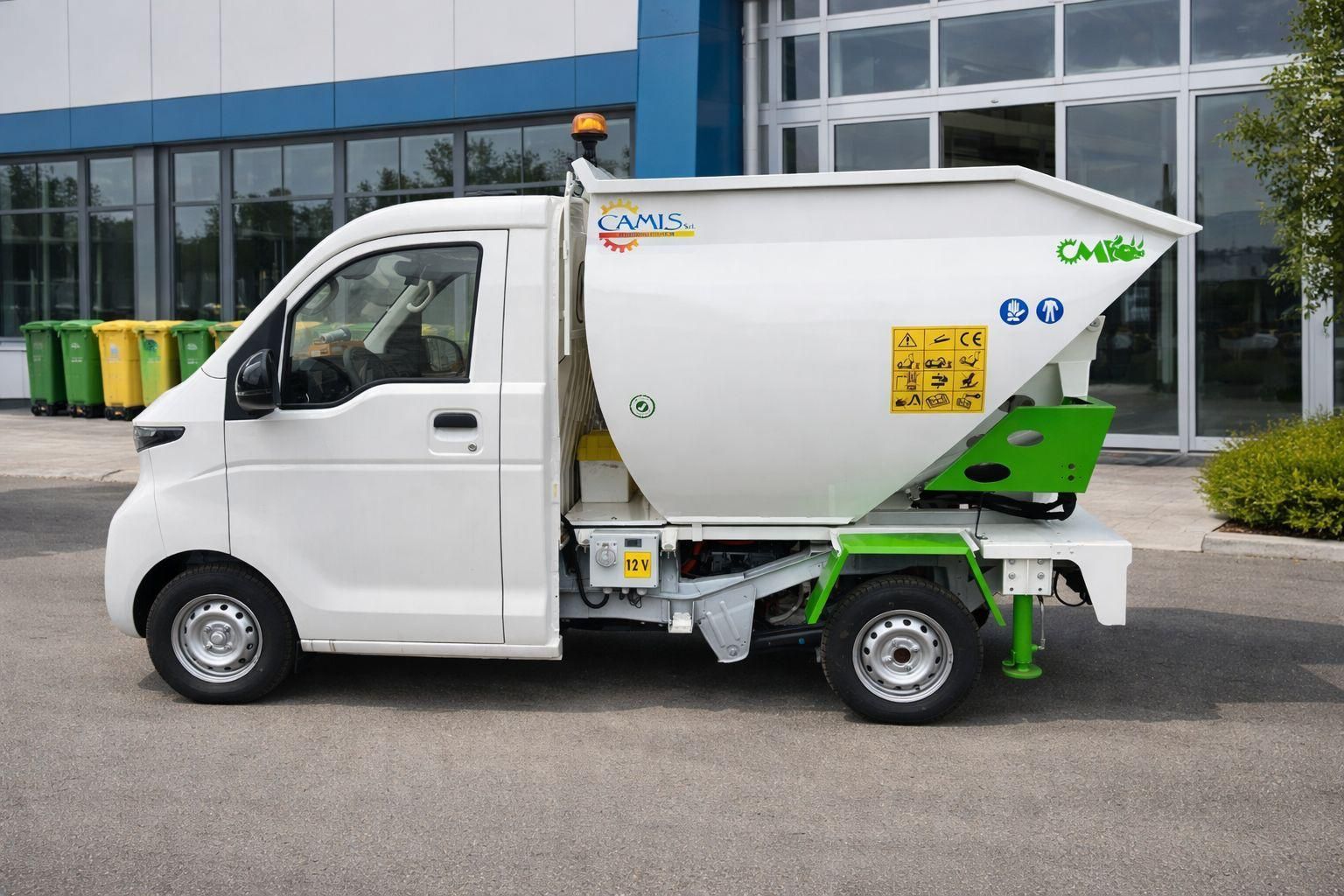 Un camioncino bianco con un grande serbatoio verde e bianco è parcheggiato davanti a un edificio con facciata in vetro.