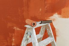 A paint roller is sitting on top of a wooden ladder.