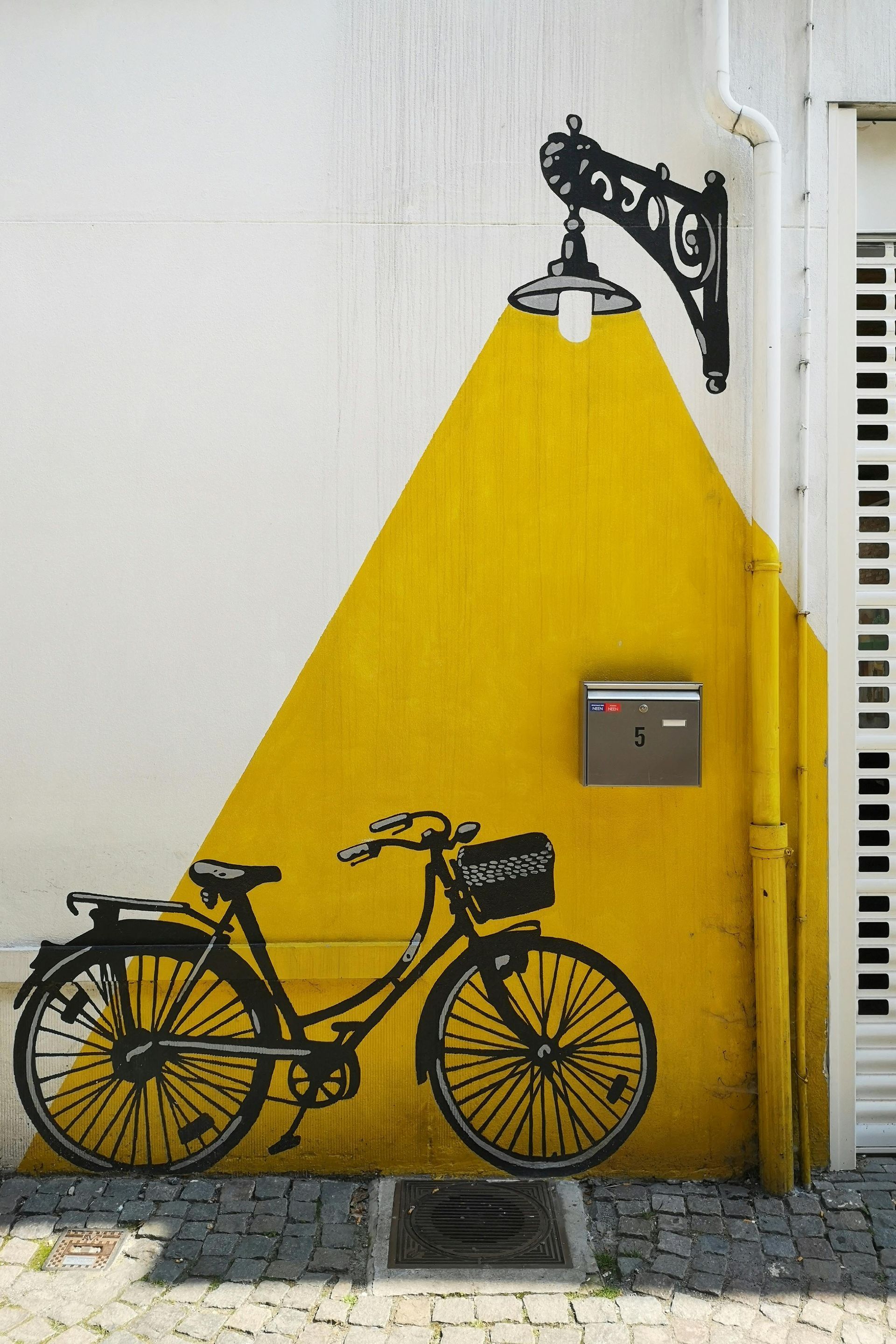 A bicycle is painted on a yellow and white wall next to a mailbox.
