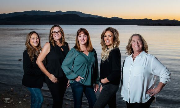 A group of women are posing for a picture in front of a lake.
