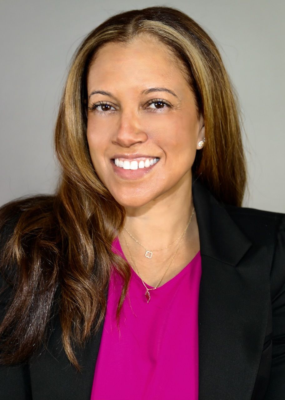 A woman wearing a pink shirt and a black jacket is smiling for the camera.