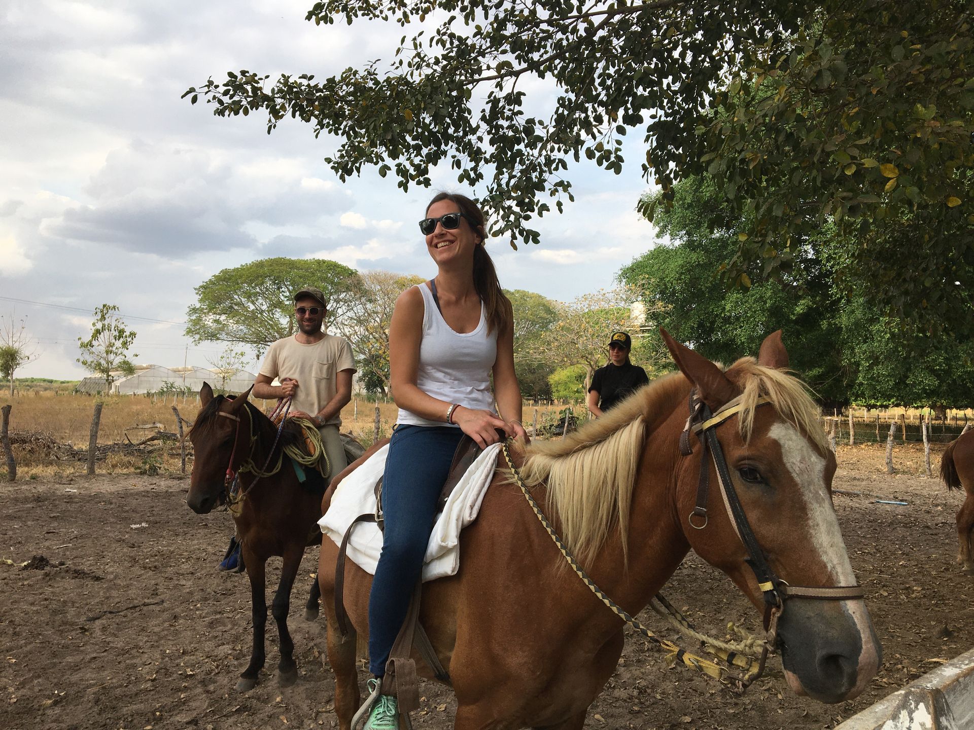 Woman on a brown horse smiles while riding with others in a rural setting.