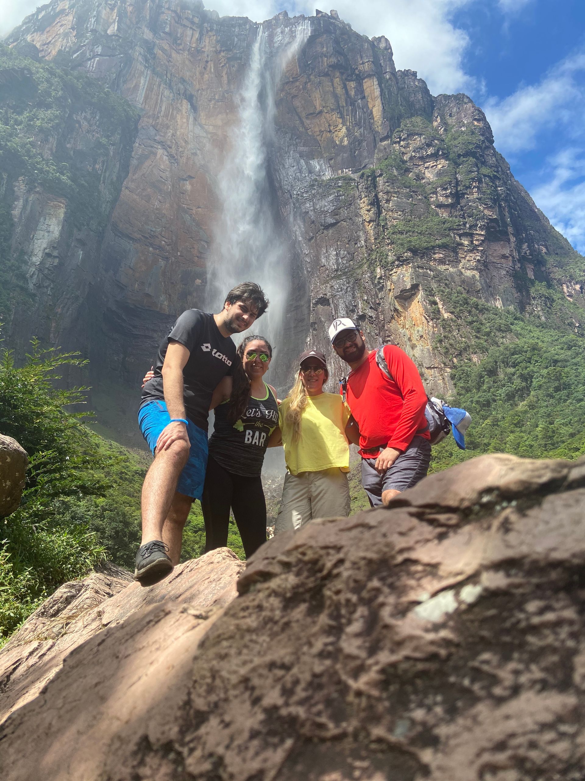 Group of four people posing in front of Angel Falls, Venezuela. Two men and two women stand on rocks with the waterfall cascading behind them.
