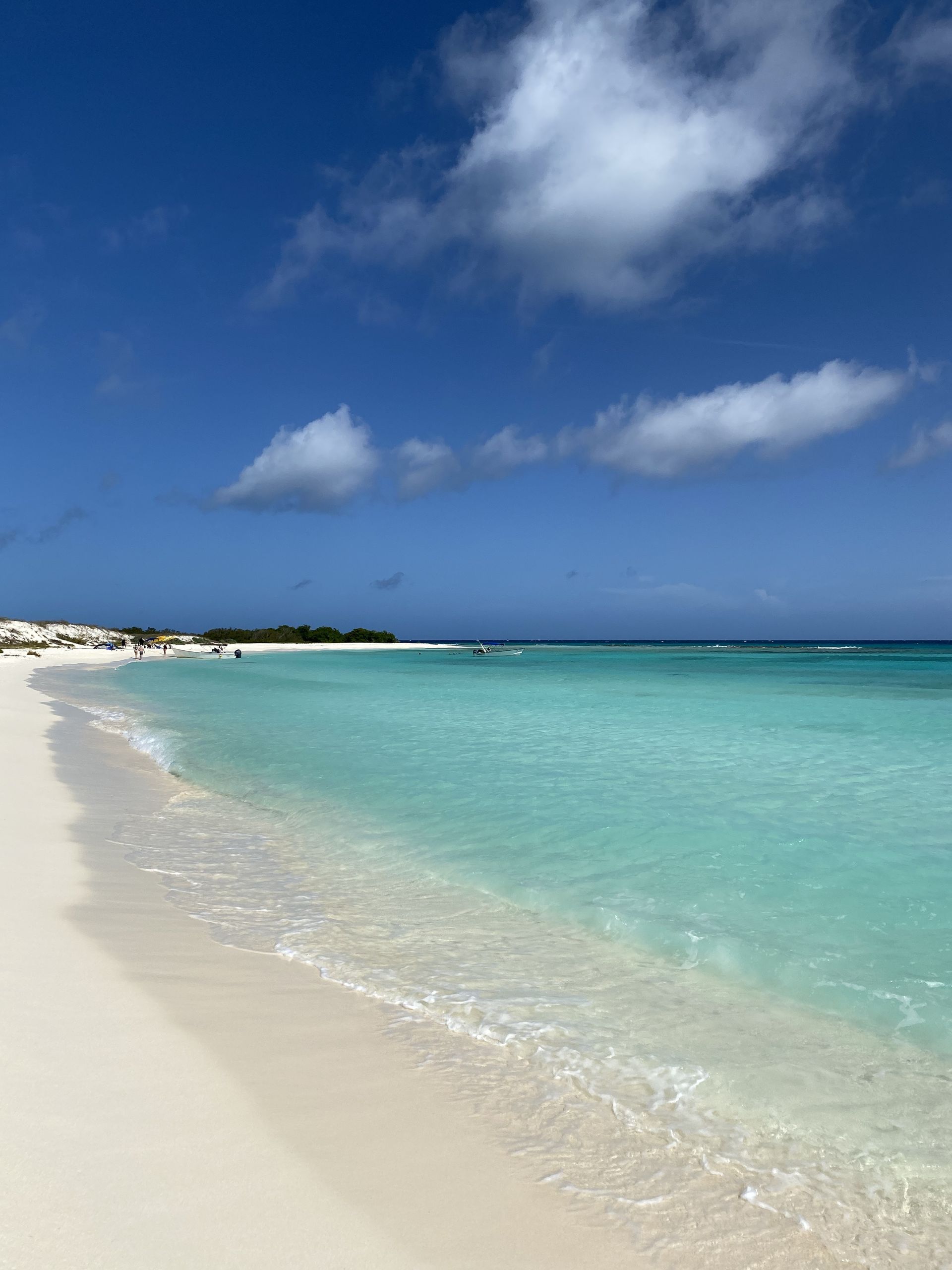 A pristine white sandy beach meets clear turquoise water under a blue sky with fluffy white clouds.