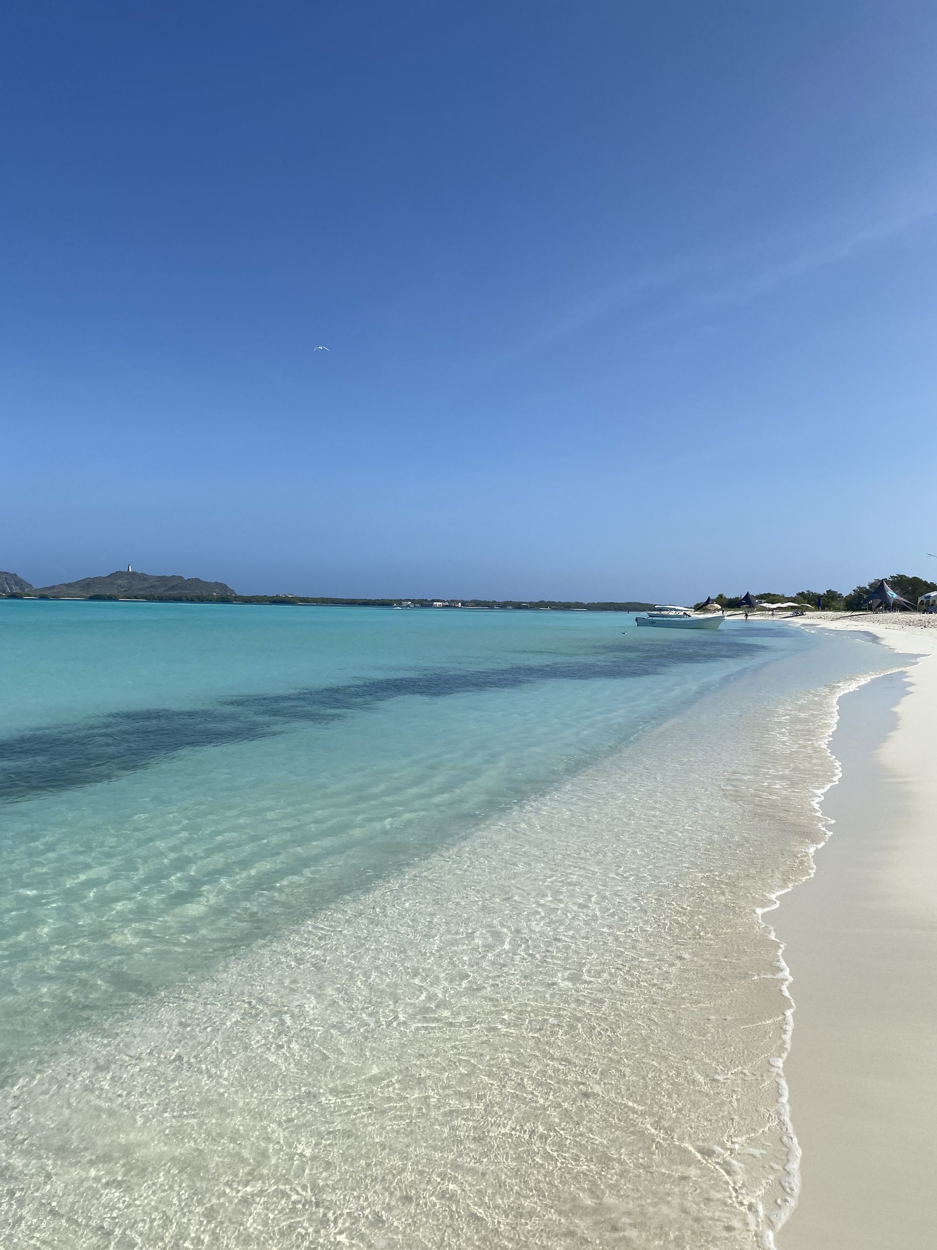 White sand beach meets crystal-clear turquoise water under a bright blue sky.