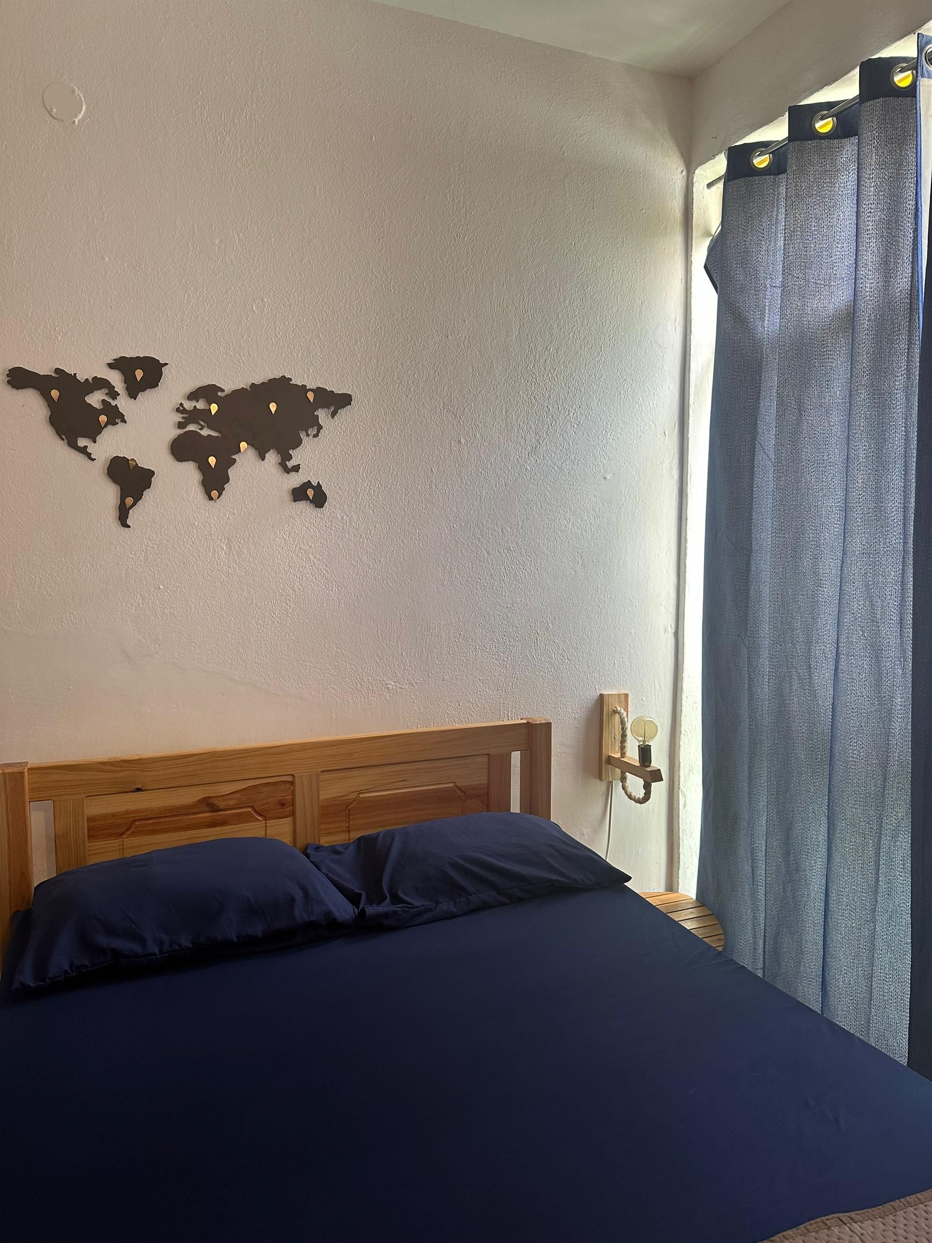 Bedroom with a wooden bed, navy blue bedding, and a world map decoration on a textured wall. Dark blue curtains are visible.