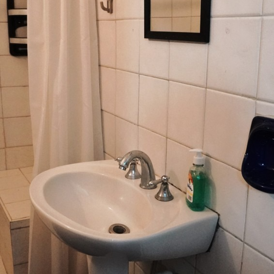 A small bathroom with a white sink, shower curtain, and tiled walls. A bottle of soap sits near the faucet.