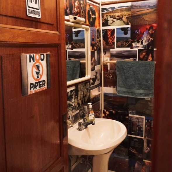 A small bathroom with the walls covered in collaged photos. A white sink, mirror, and a