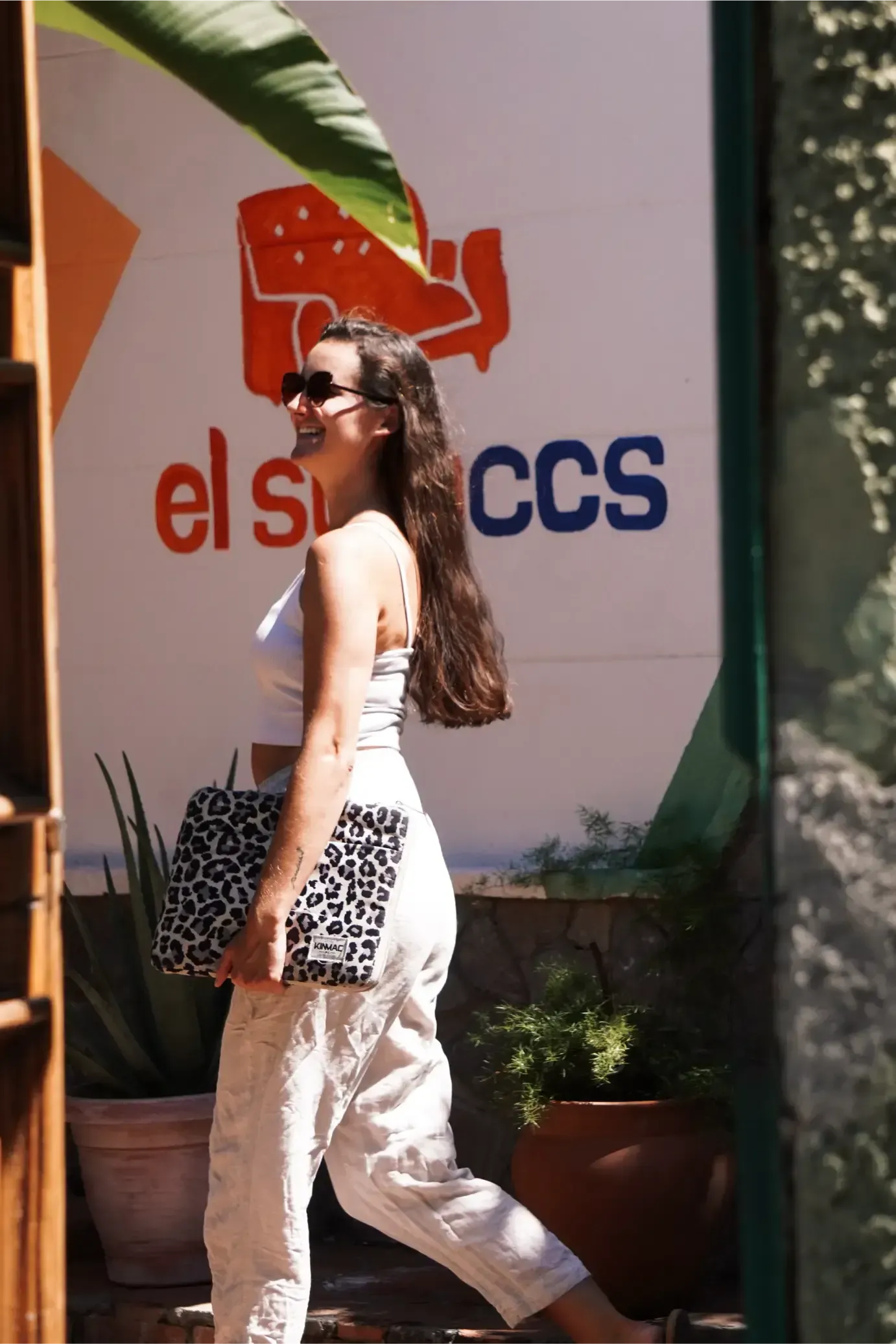 Woman in sunglasses exits a building, holding a leopard-print clutch. The sign above reads