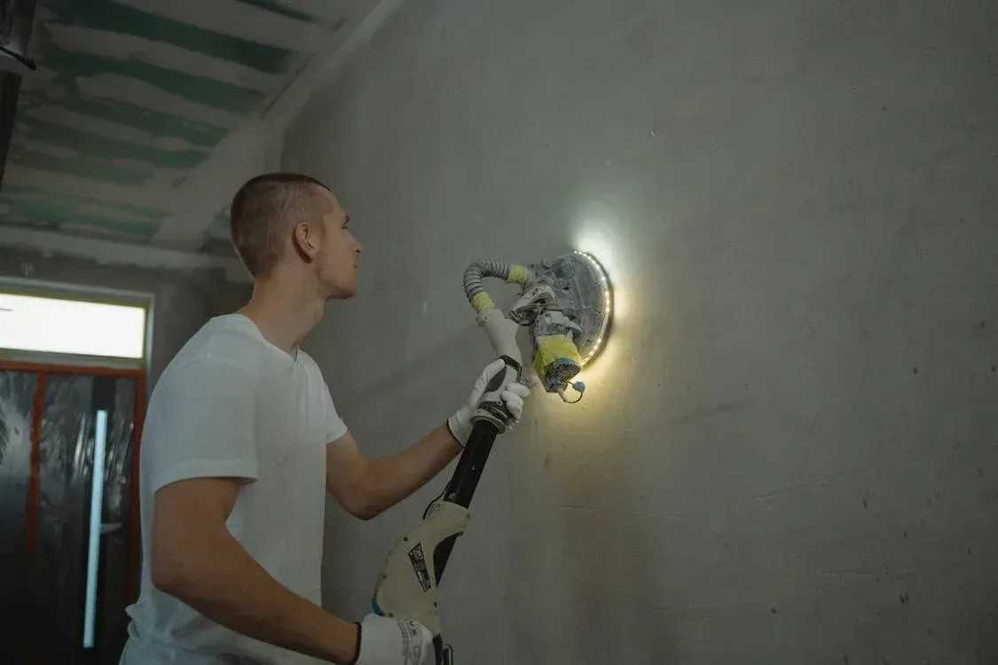A man is using a machine to sand a wall.