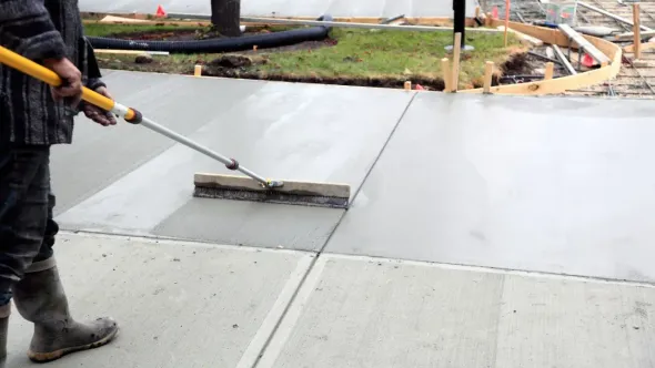 A man is spreading concrete on a sidewalk with a broom.