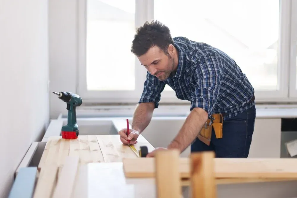 A man is measuring a piece of wood with a tape measure.