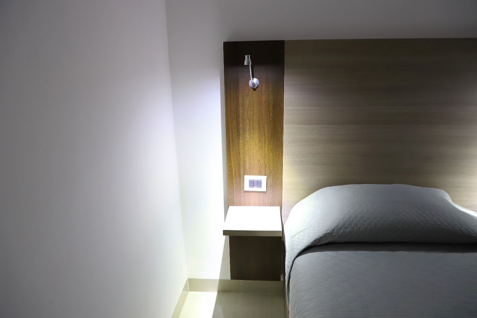 Un dormitorio con una cama, mesita de noche y luz en la pared.