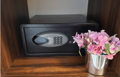 Una caja fuerte está sobre un estante de madera al lado de un jarrón con flores.