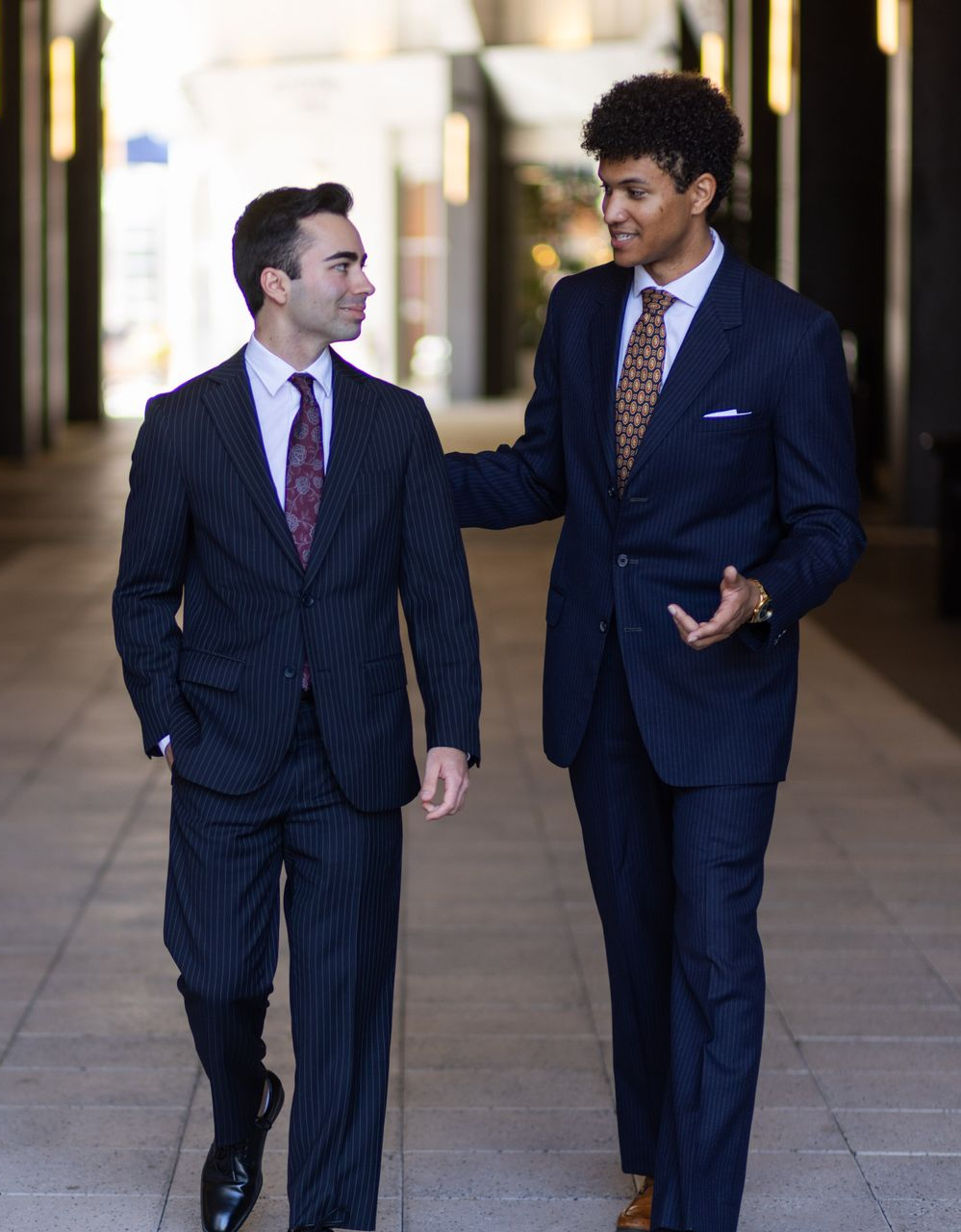 Two men in pinstripe suits walking and talking in an outdoor walkway.
