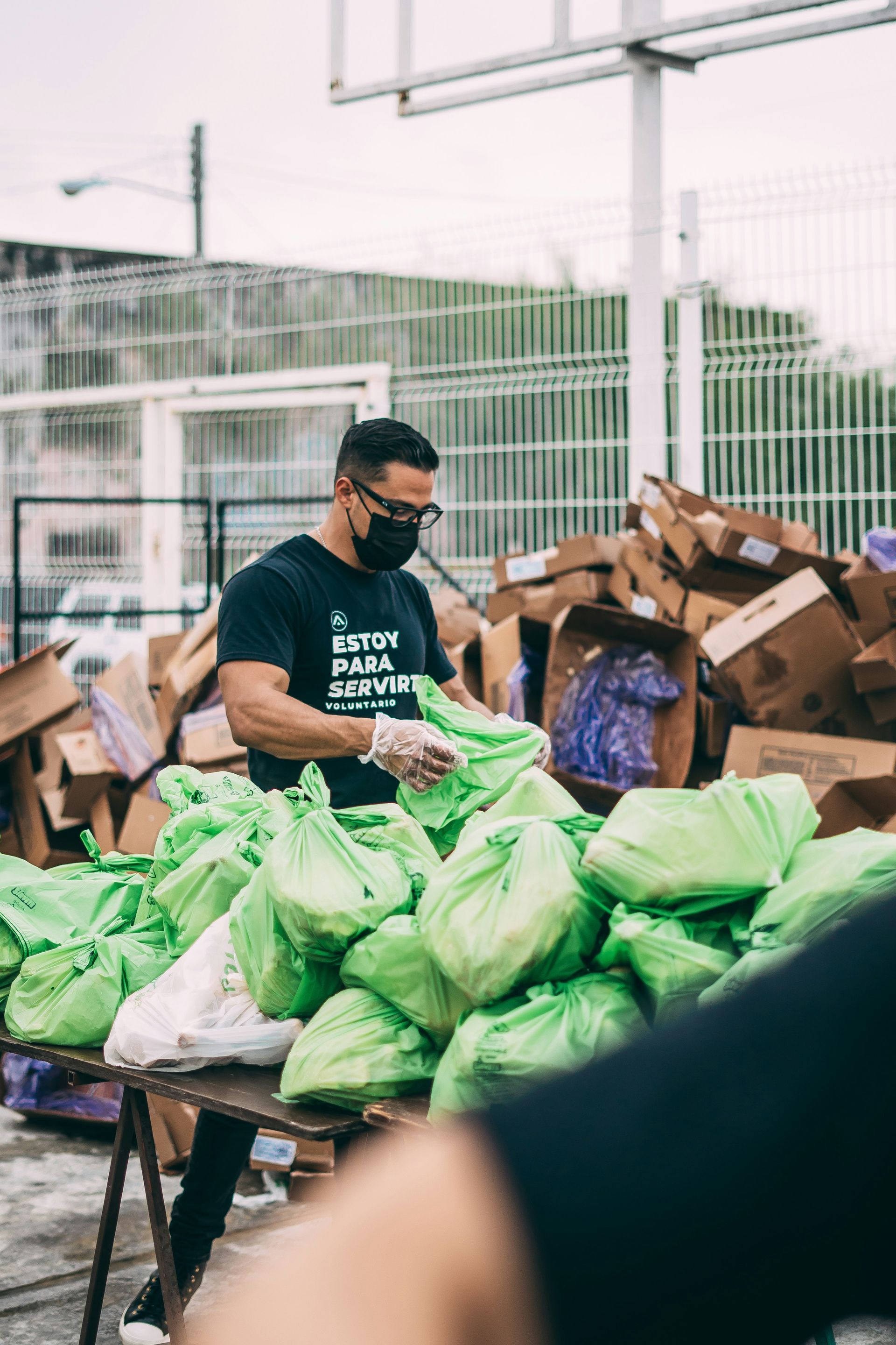 Man in mask and gloves packs bags of food outdoors, next to boxes.