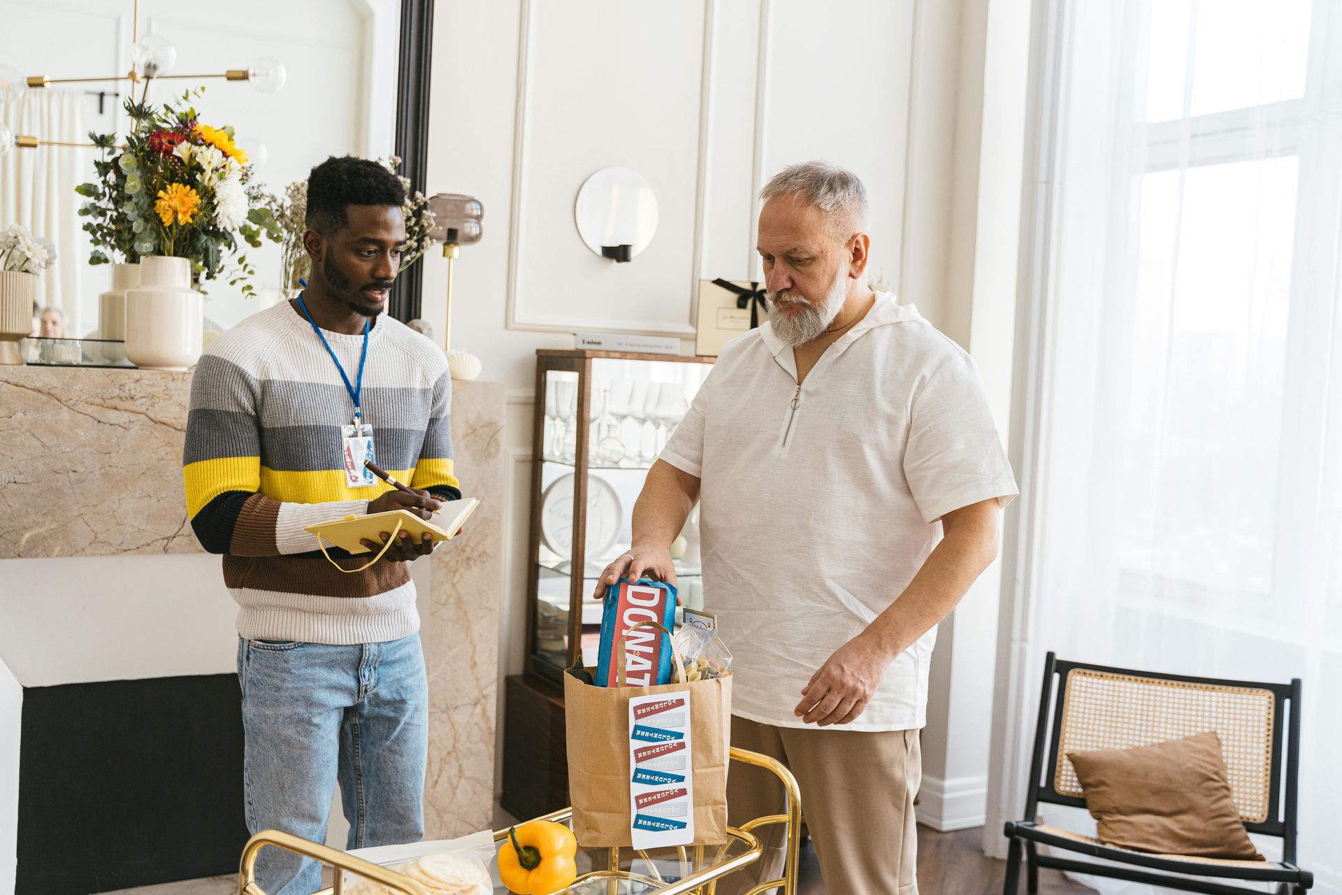 Man delivering groceries to an older man in a living room.