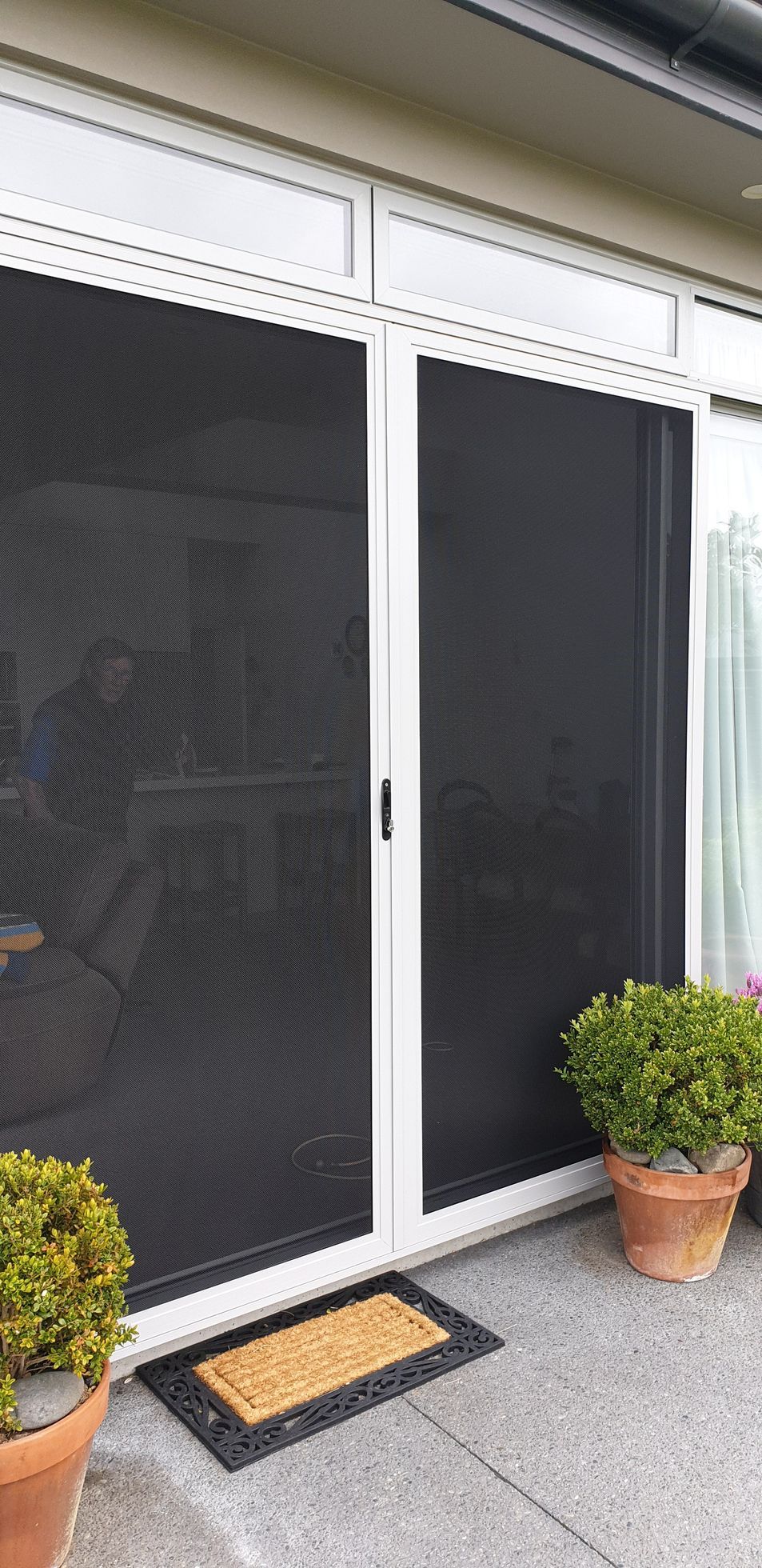 A white screen door is open to a living room with a table and chairs.